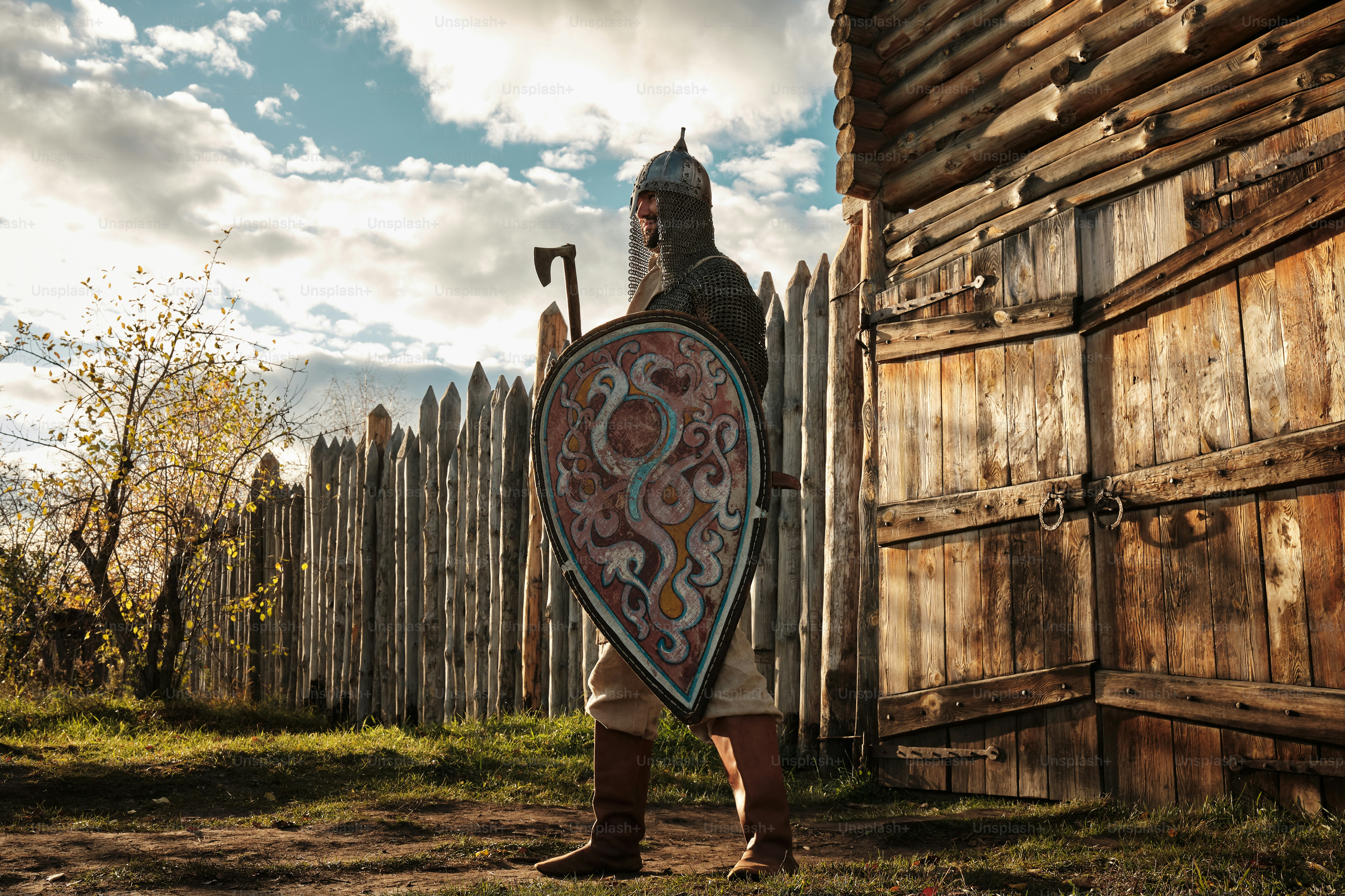 Portrait of a medieval guard with a spear near a wooden gate of a medieval settlement
