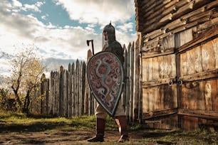 Un hombre de pie junto a una valla de madera sosteniendo un escudo