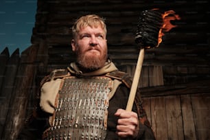 Un hombre vestido con armadura sosteniendo un palo de fuego