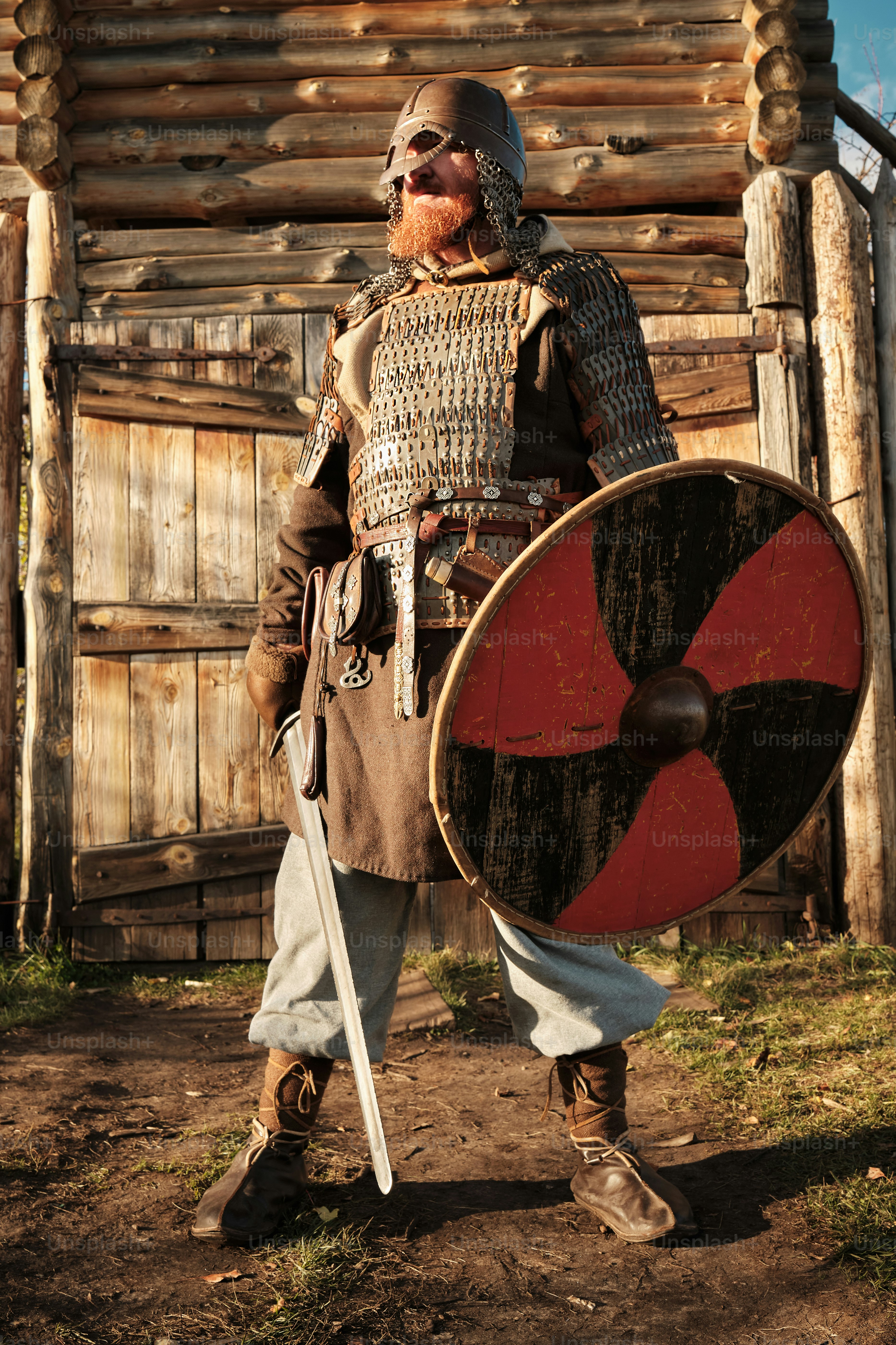 Portrait of a medieval guard with a spear near a wooden gate of a medieval settlement