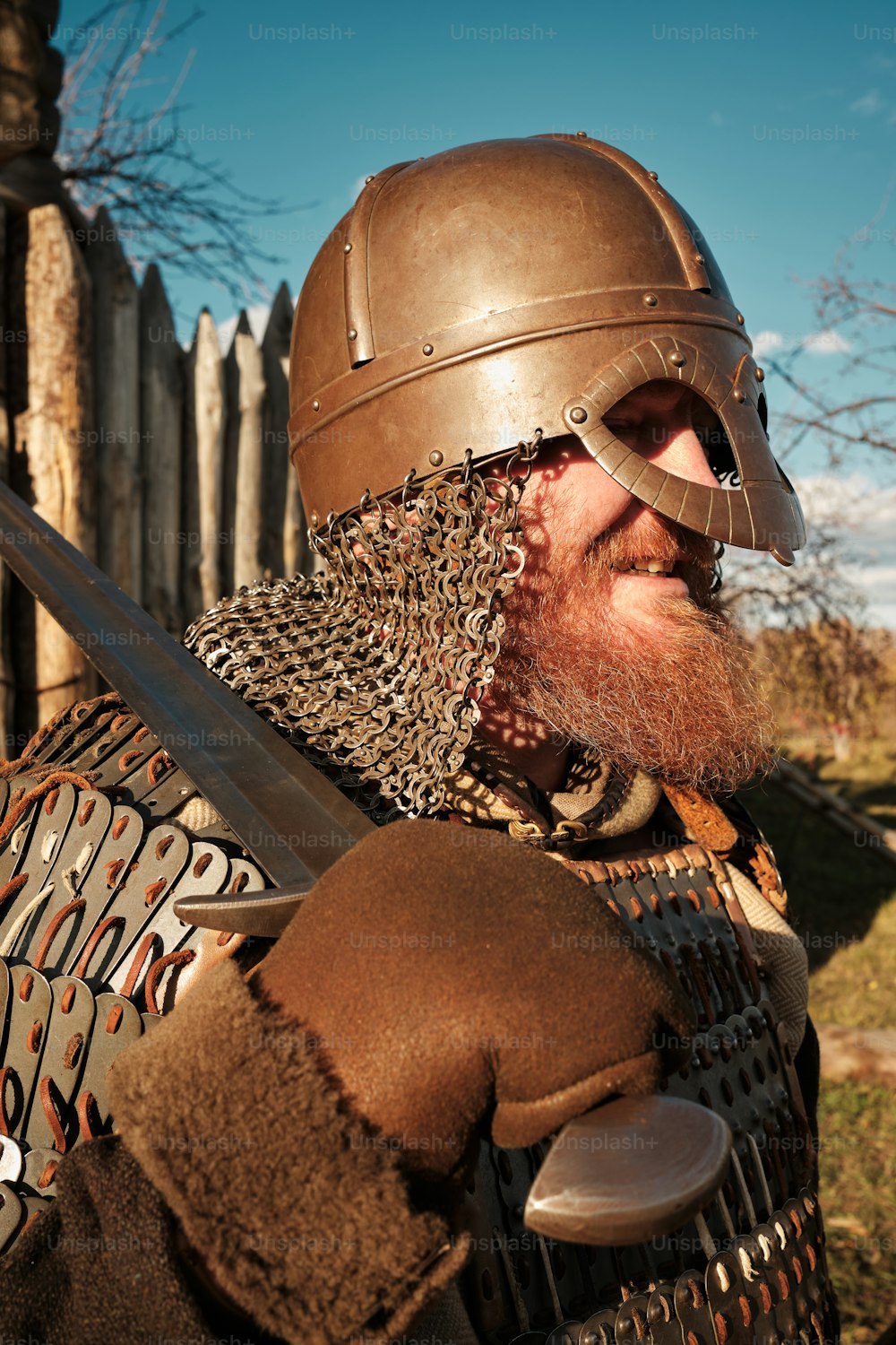 Un hombre con barba que lleva un casco y sostiene una espada