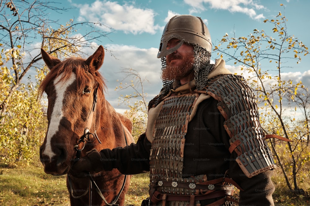 Un hombre con armadura de pie junto a un caballo