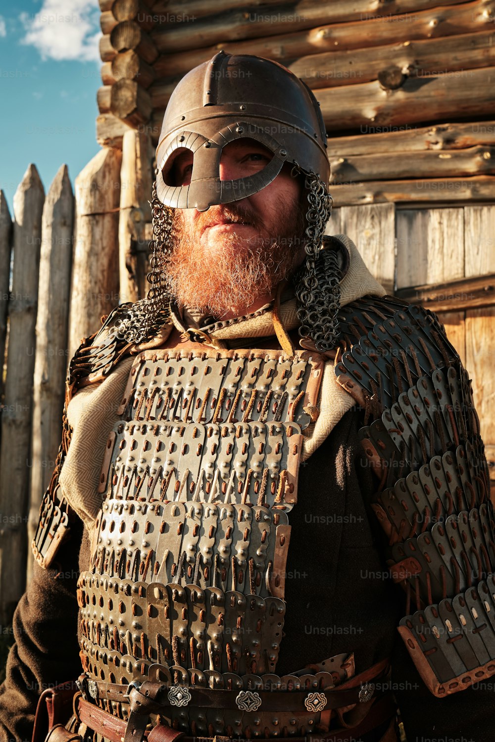 a man wearing a helmet and armor standing in front of a wooden fence