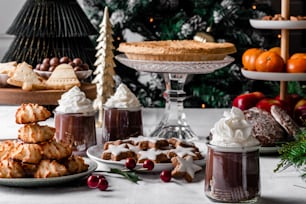 Una mesa cubierta con pasteles y postres junto a un árbol de Navidad