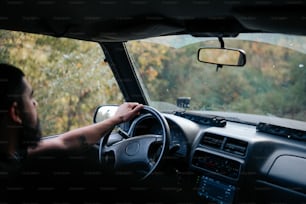 a man driving a car on a road next to a forest
