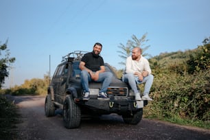 two men sitting on the back of a pick up truck