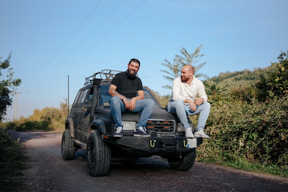 two men sitting on the back of a pick up truck