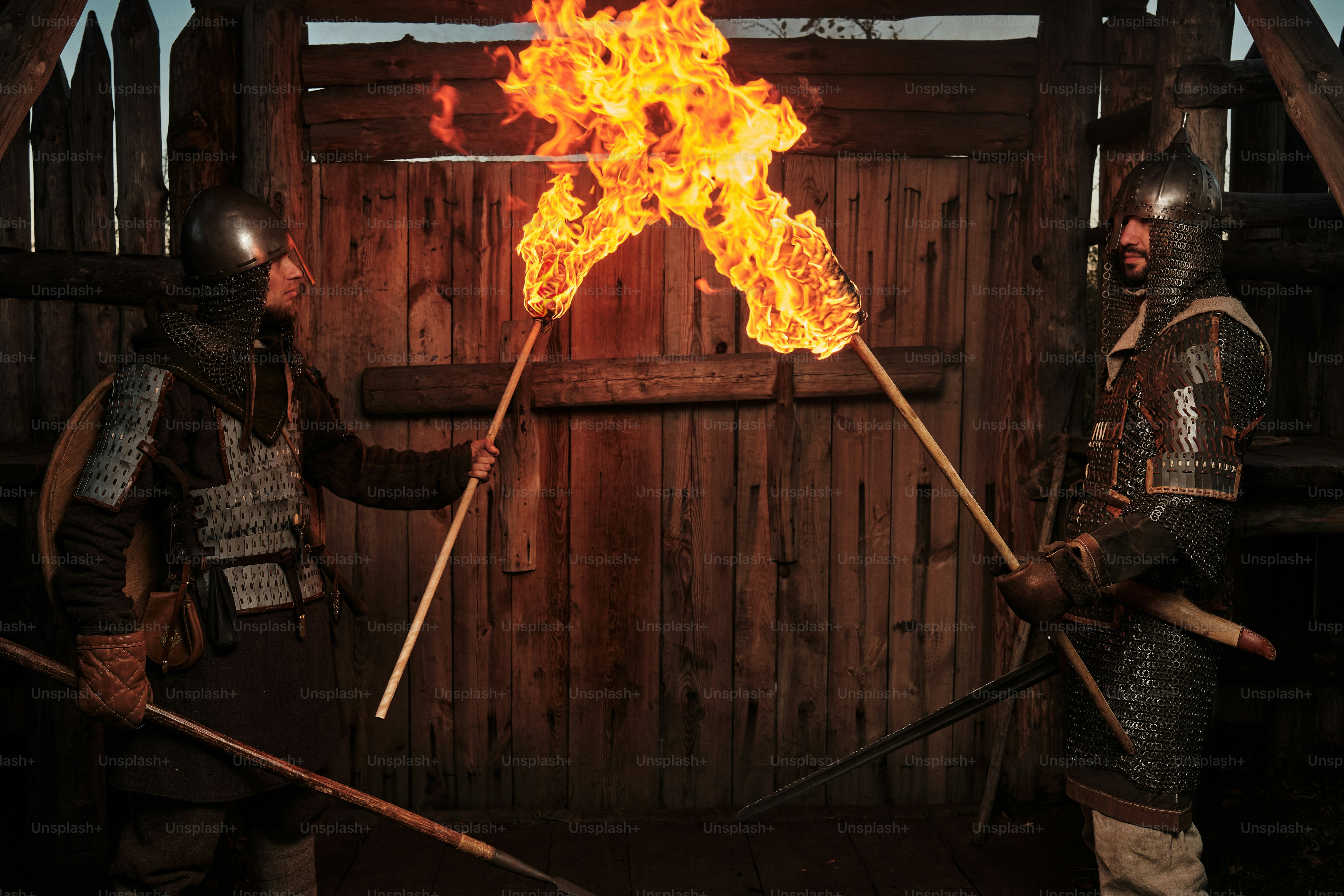 two medieval guards with torches near a wooden gate