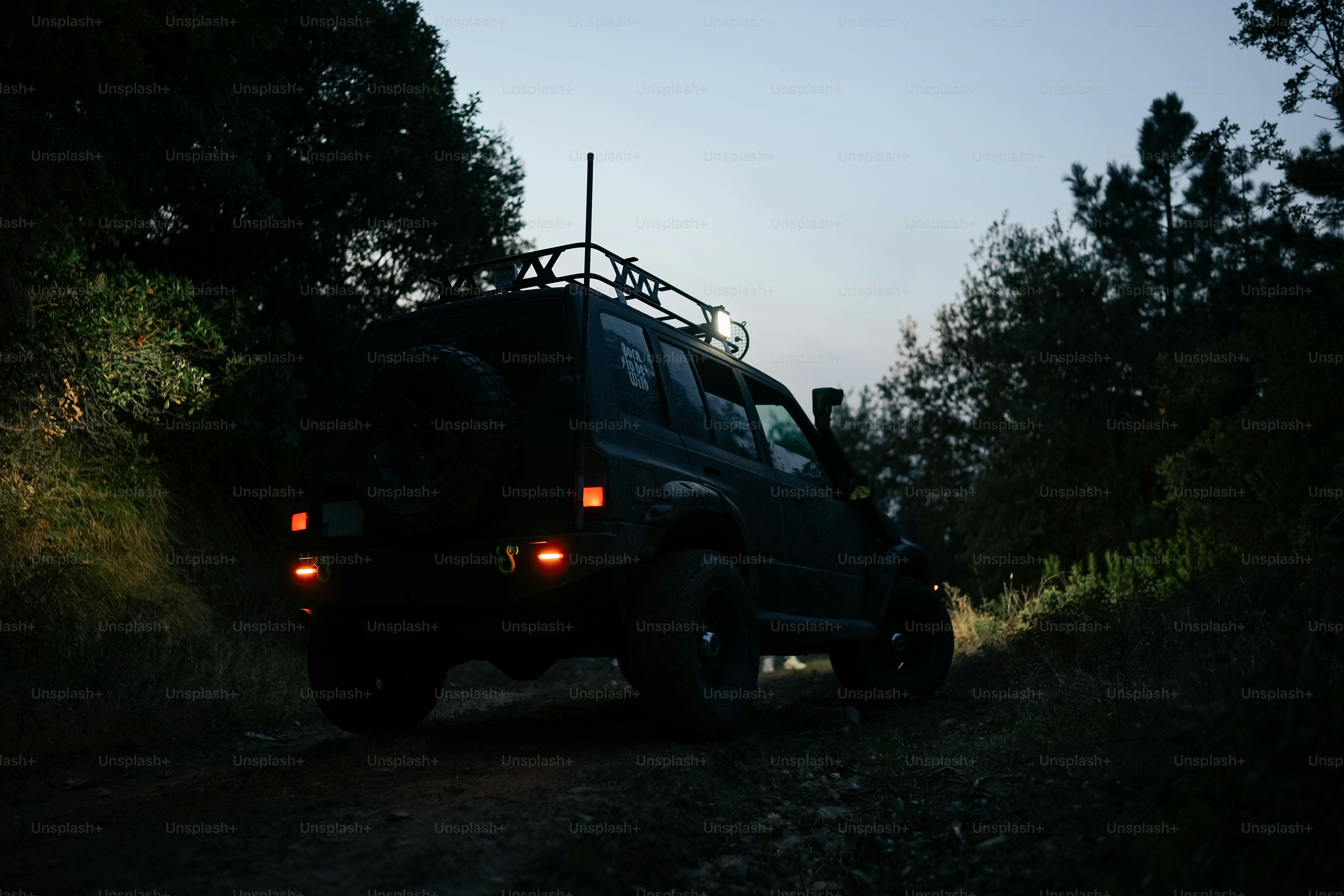 a jeep driving down a dirt road next to a forest
