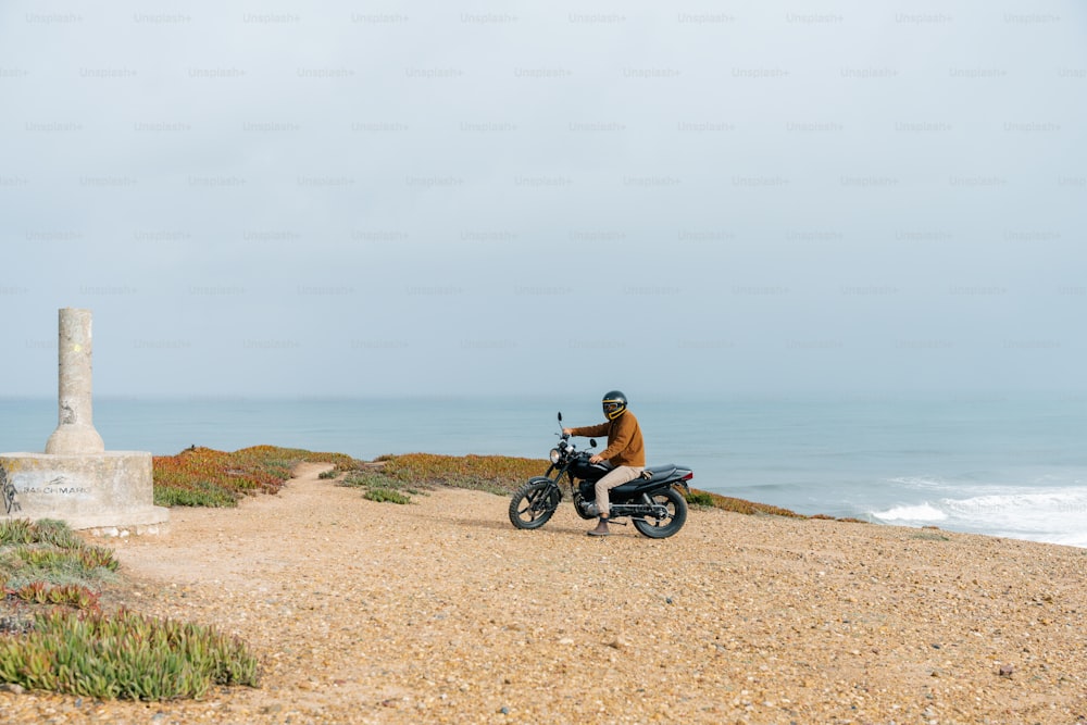 a man riding a motorcycle down a dirt road next to the ocean
