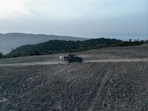 two people standing next to a car on a dirt road