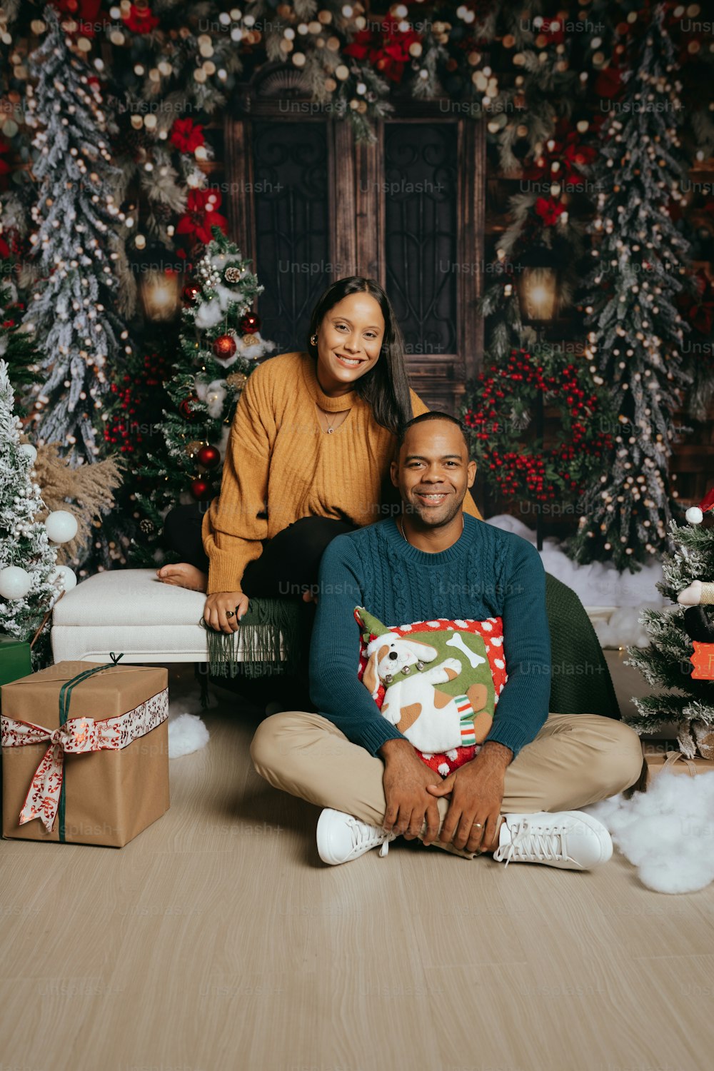 a man and woman sitting on the floor in front of christmas trees