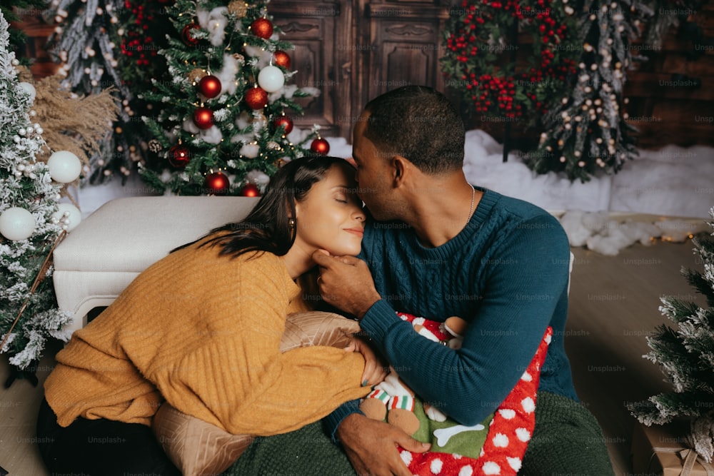a man and a woman cuddle in front of a christmas tree