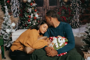 a man and woman sitting on a couch in front of christmas trees