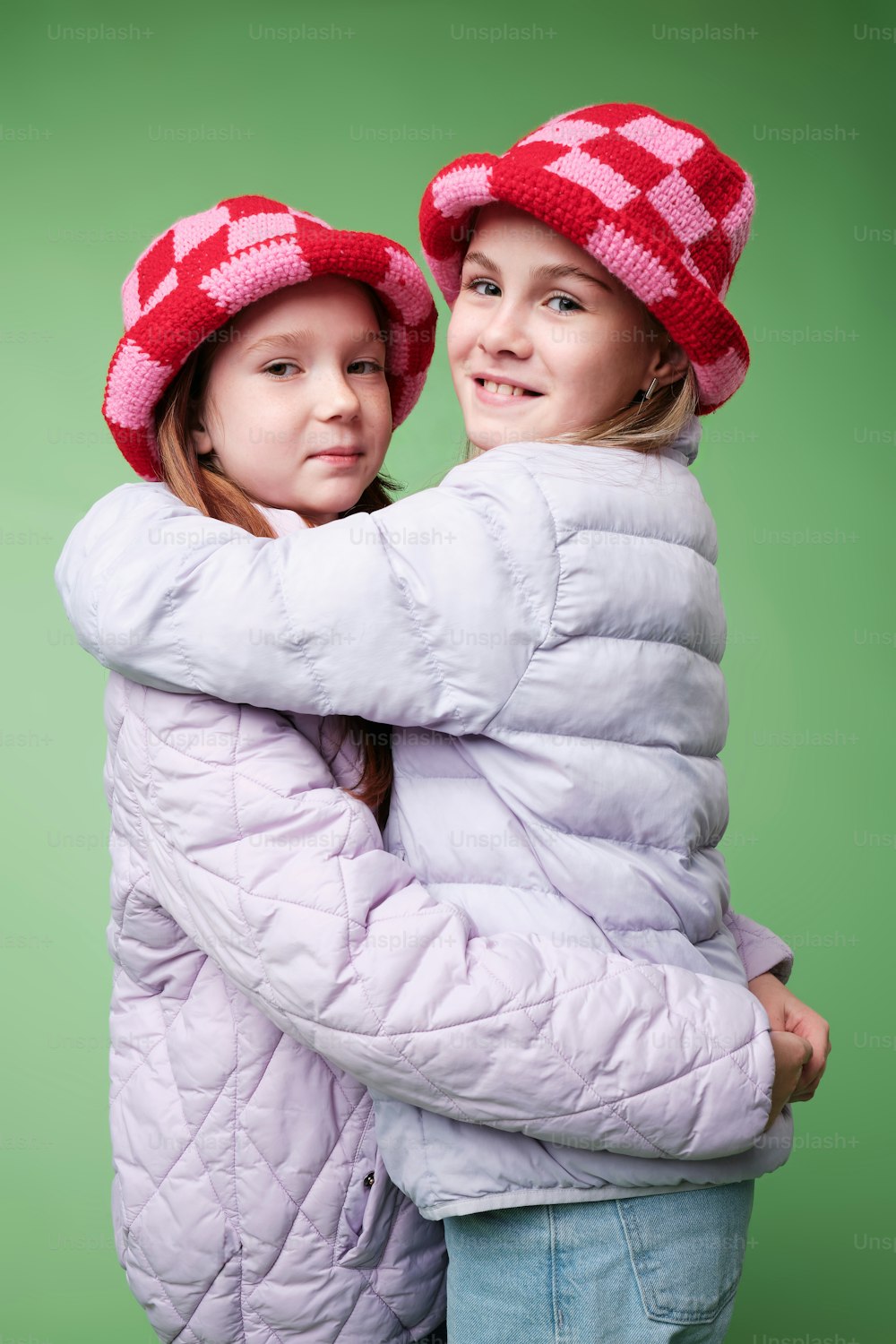 two young girls are hugging each other while wearing hats