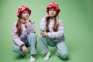 two young girls sitting on the ground wearing hats