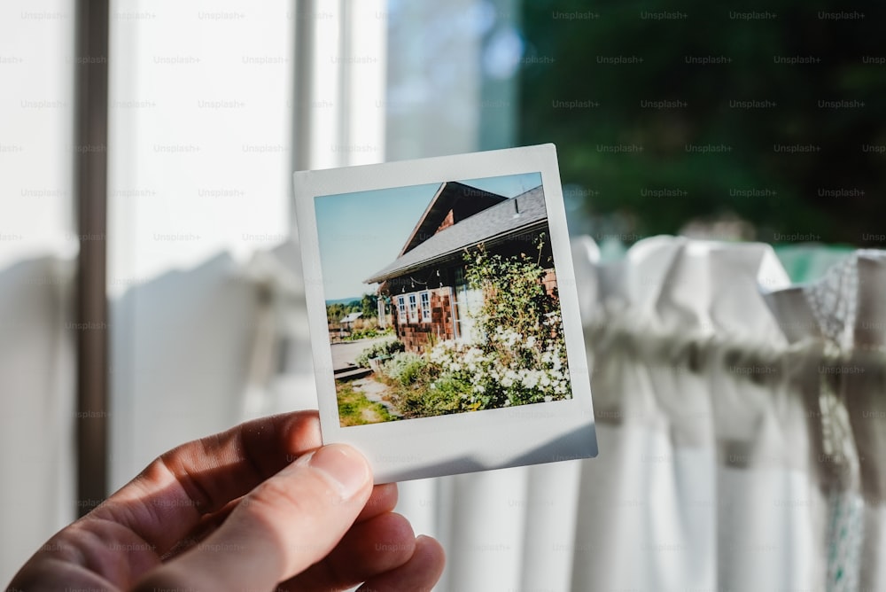 a person holding up a polaroid picture of a house