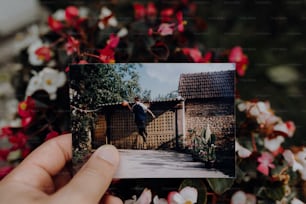 a person holding up a polaroid picture of a person in a garden