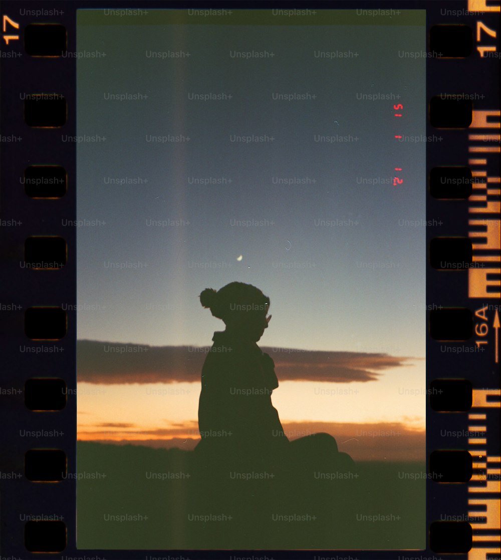 die Silhouette einer Person, die vor einem Sonnenuntergang sitzt