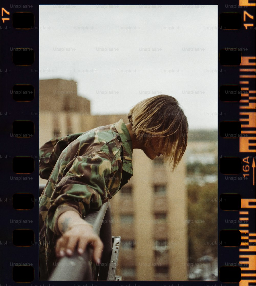 un homme en chemise de camouflage accoudé à une balustrade