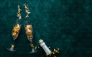 two champagne flutes filled with gold confetti next to a bottle of champagne