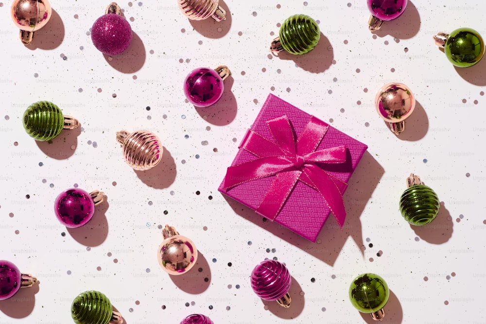 Una confezione regalo rosa con un fiocco rosa circondato da ornamenti natalizi