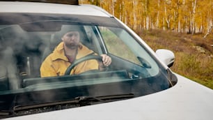 Un hombre con chaqueta amarilla conduciendo un coche blanco