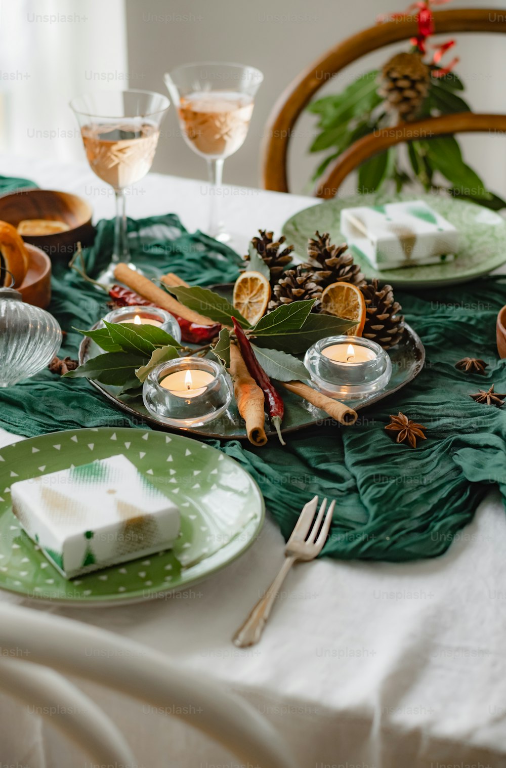 a table set for a holiday dinner with pine cones and candles