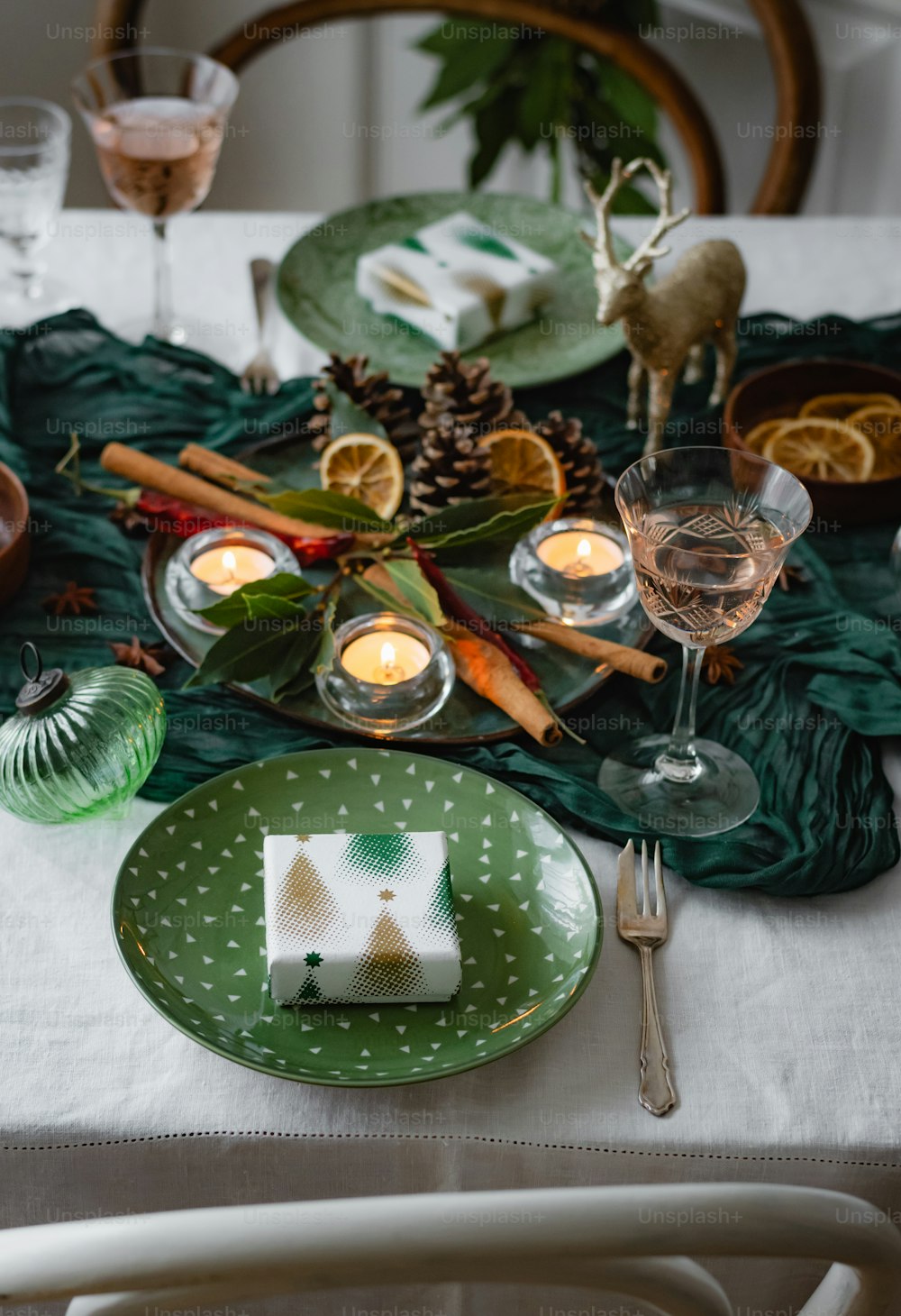 a table set for a holiday dinner with pine cones, oranges, and candles