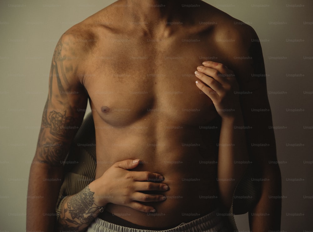 Ein Mann mit einem tätowierten Arm hält sich die Brust