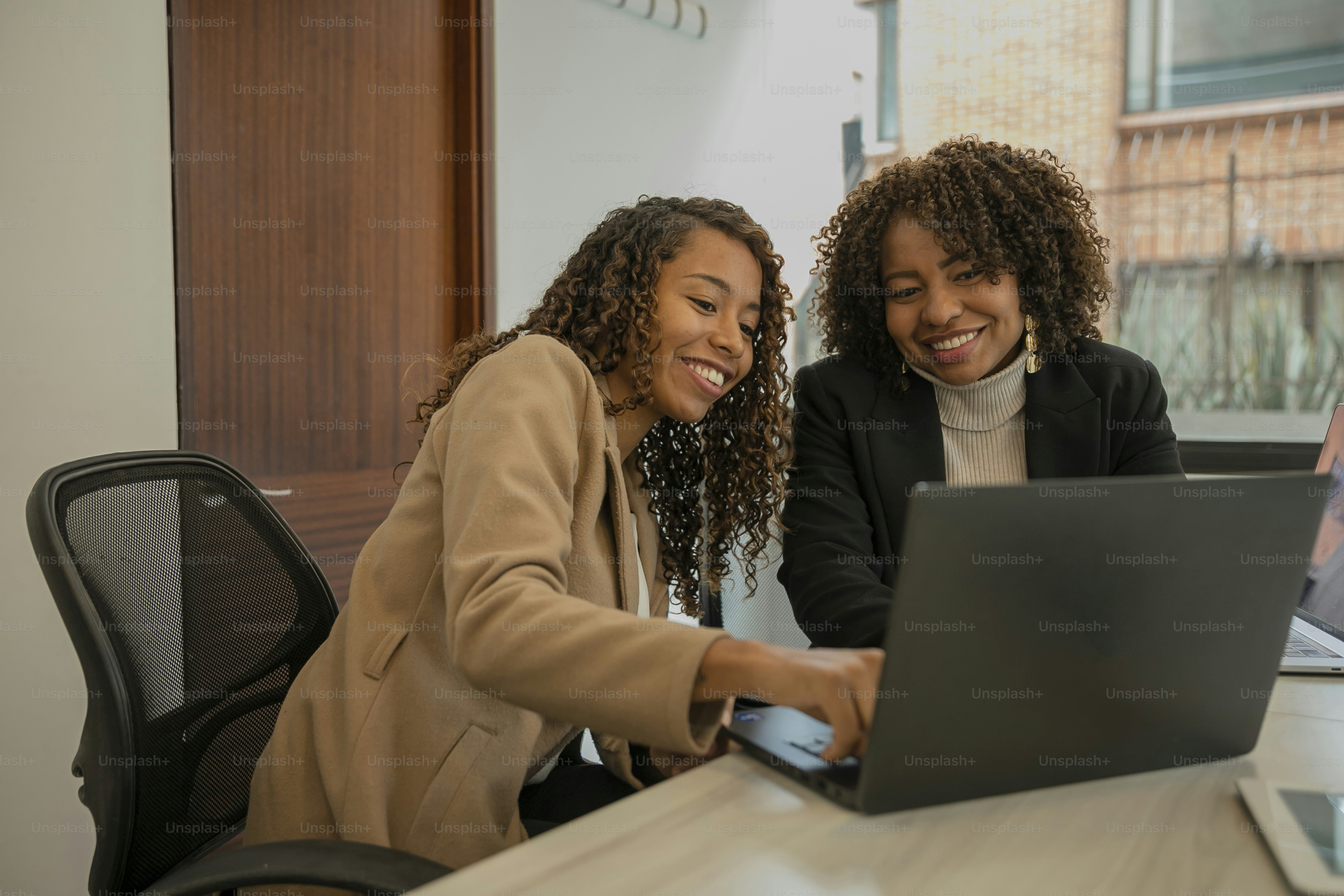 zwei Frauen sitzen an einem Tisch und schauen auf einen Laptop