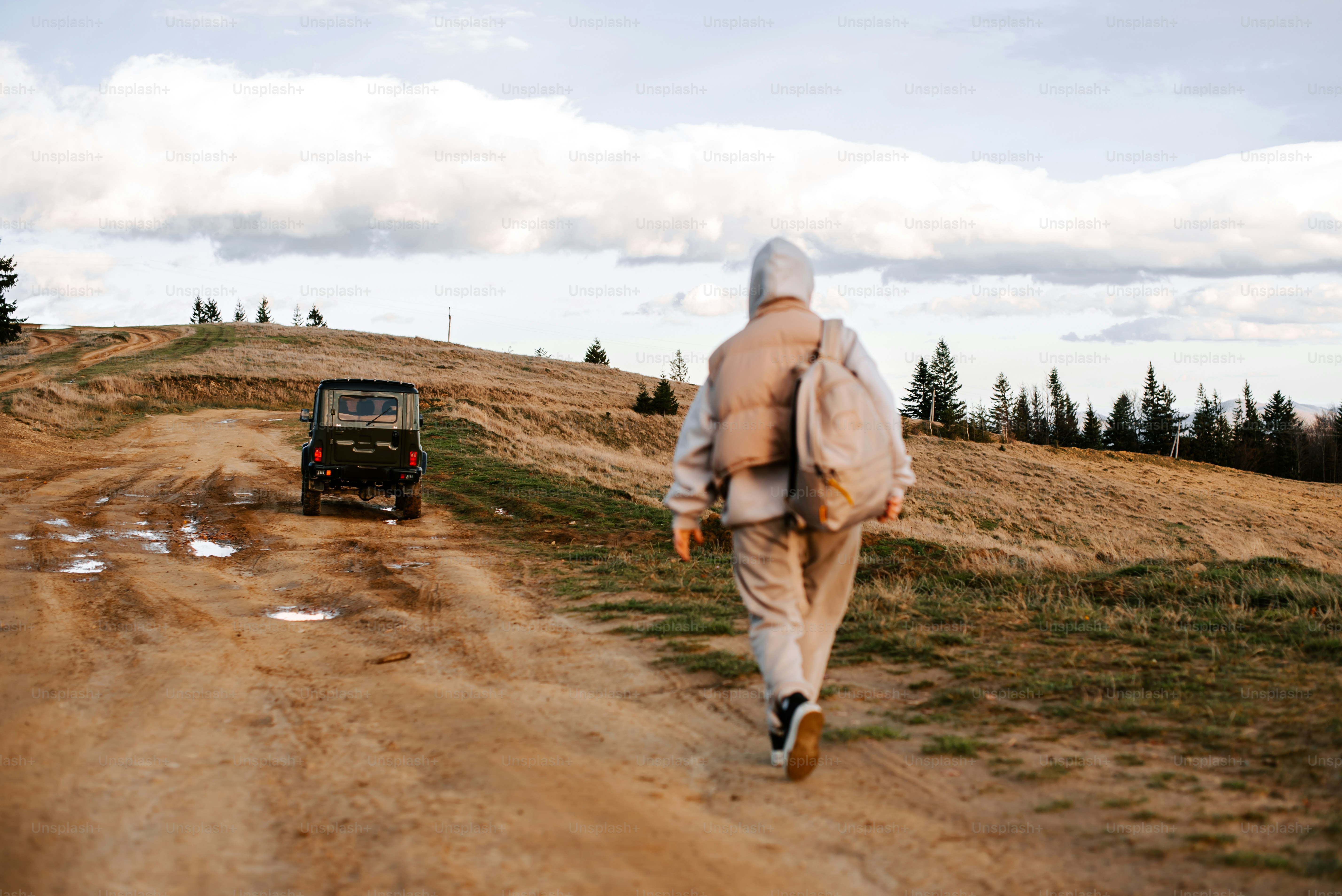 a man walking down a dirt road next to a jeep