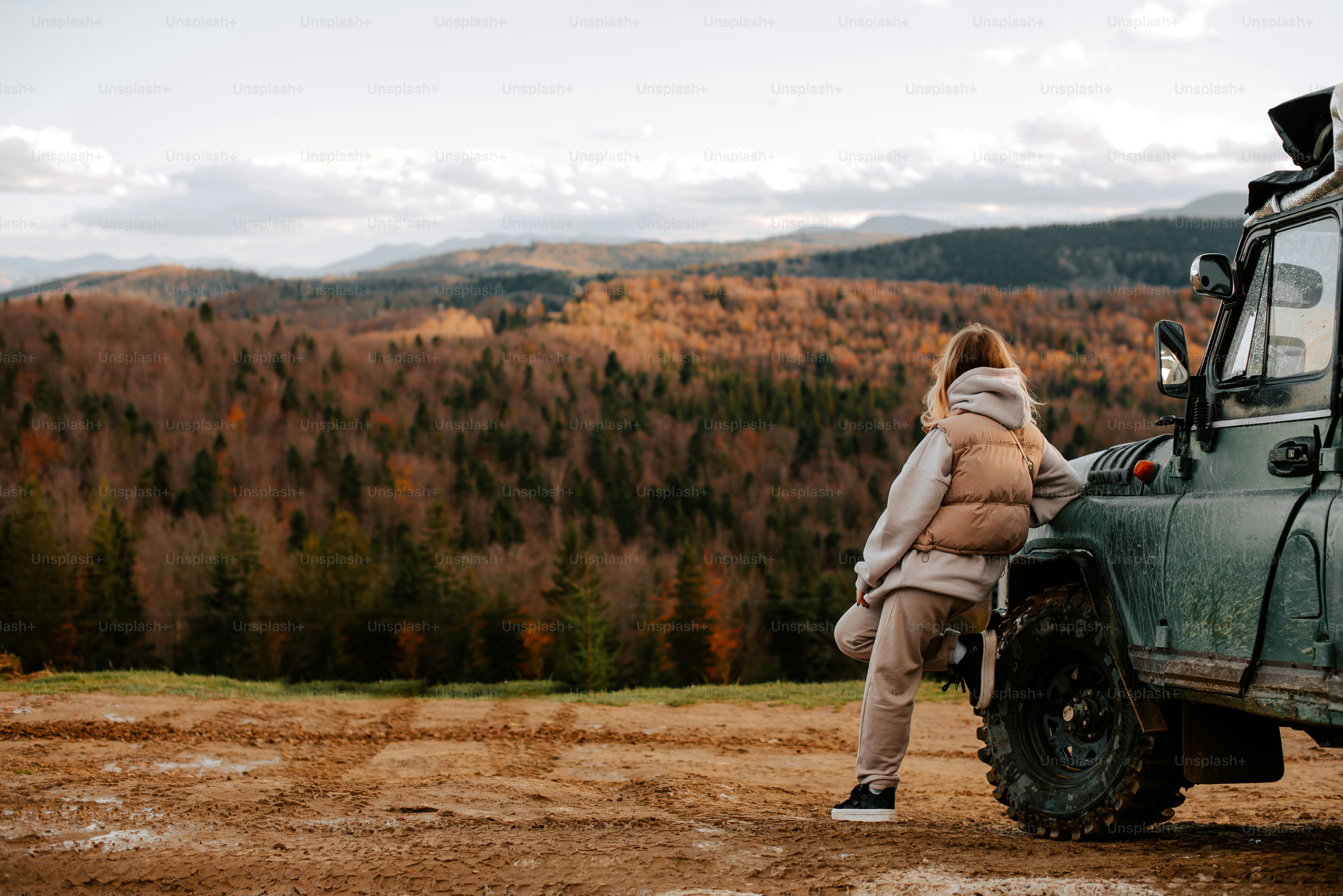 a woman leaning against a vehicle on a dirt road