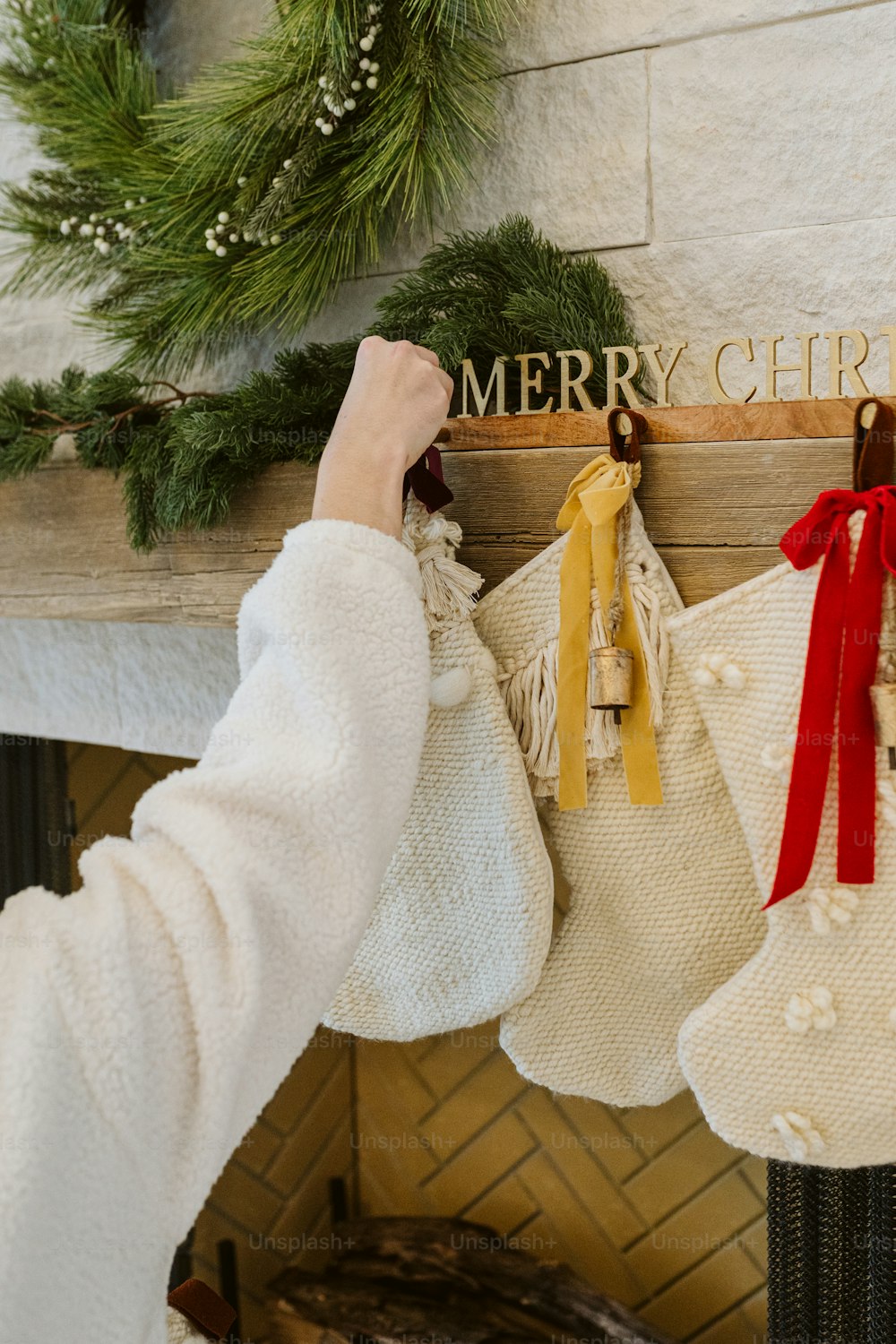a person hanging stockings on a fireplace with a merry christmas sign