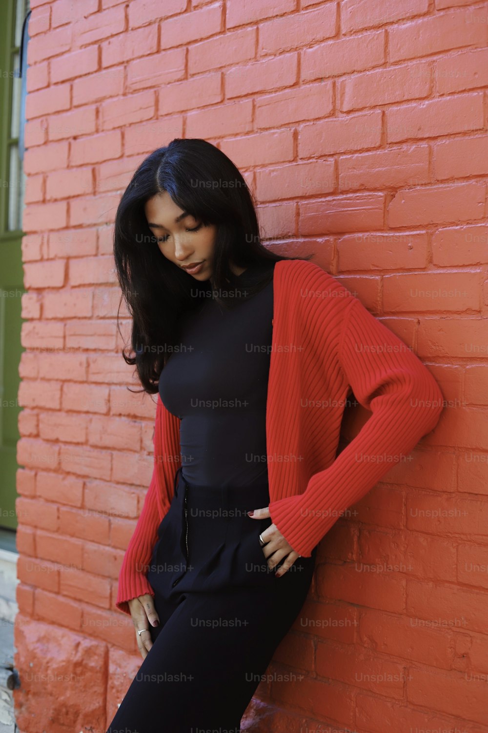 a woman leaning against a red brick wall