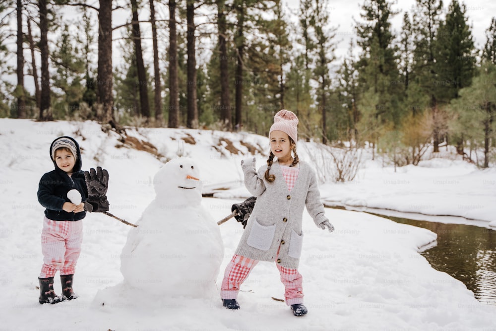 deux enfants debout à côté d’un bonhomme de neige dans la neige