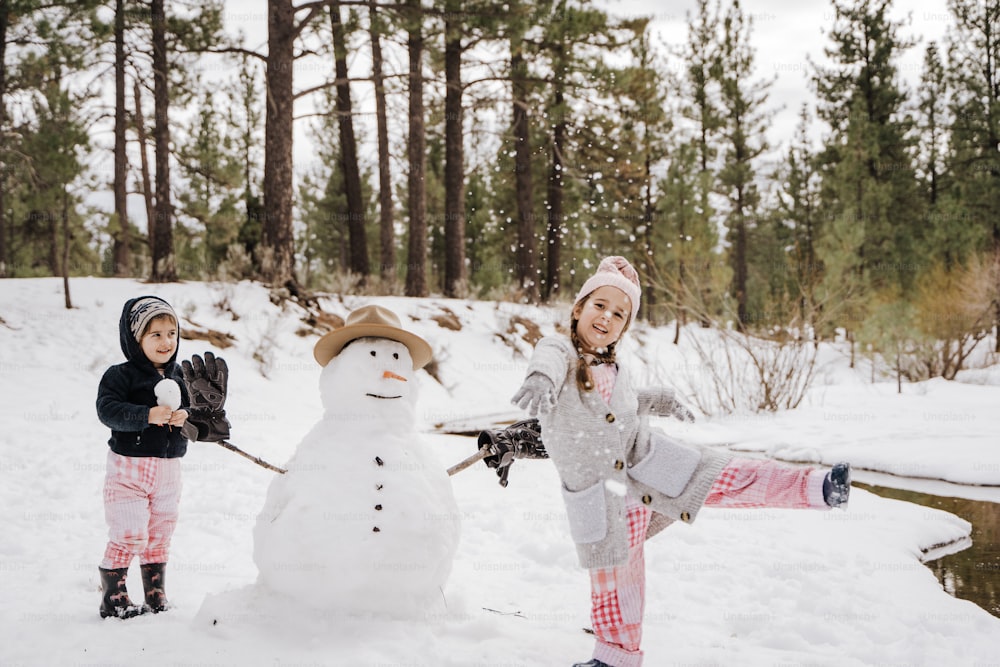 zwei kleine Mädchen, die neben einem Schneemann im Schnee stehen