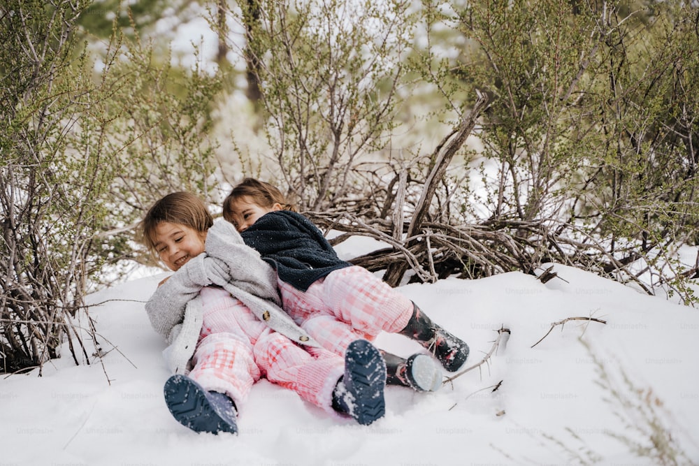 zwei kleine Mädchen, die zusammen im Schnee sitzen