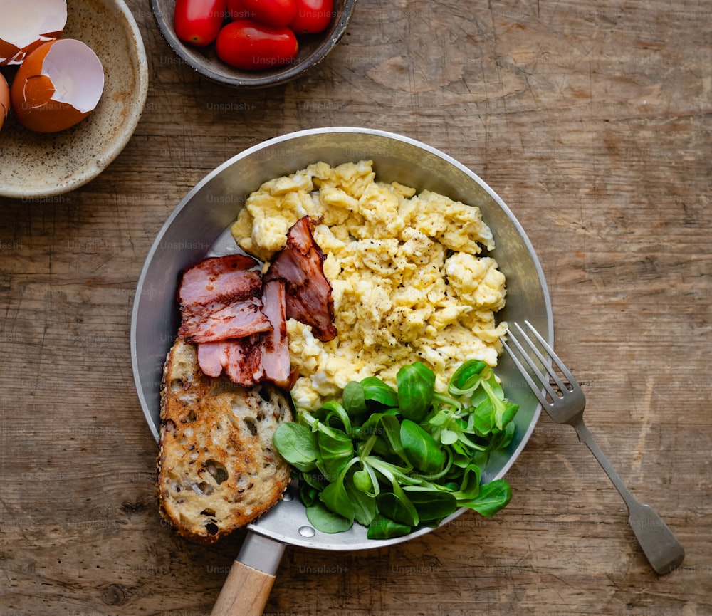a plate of eggs, bacon, and spinach on a wooden table