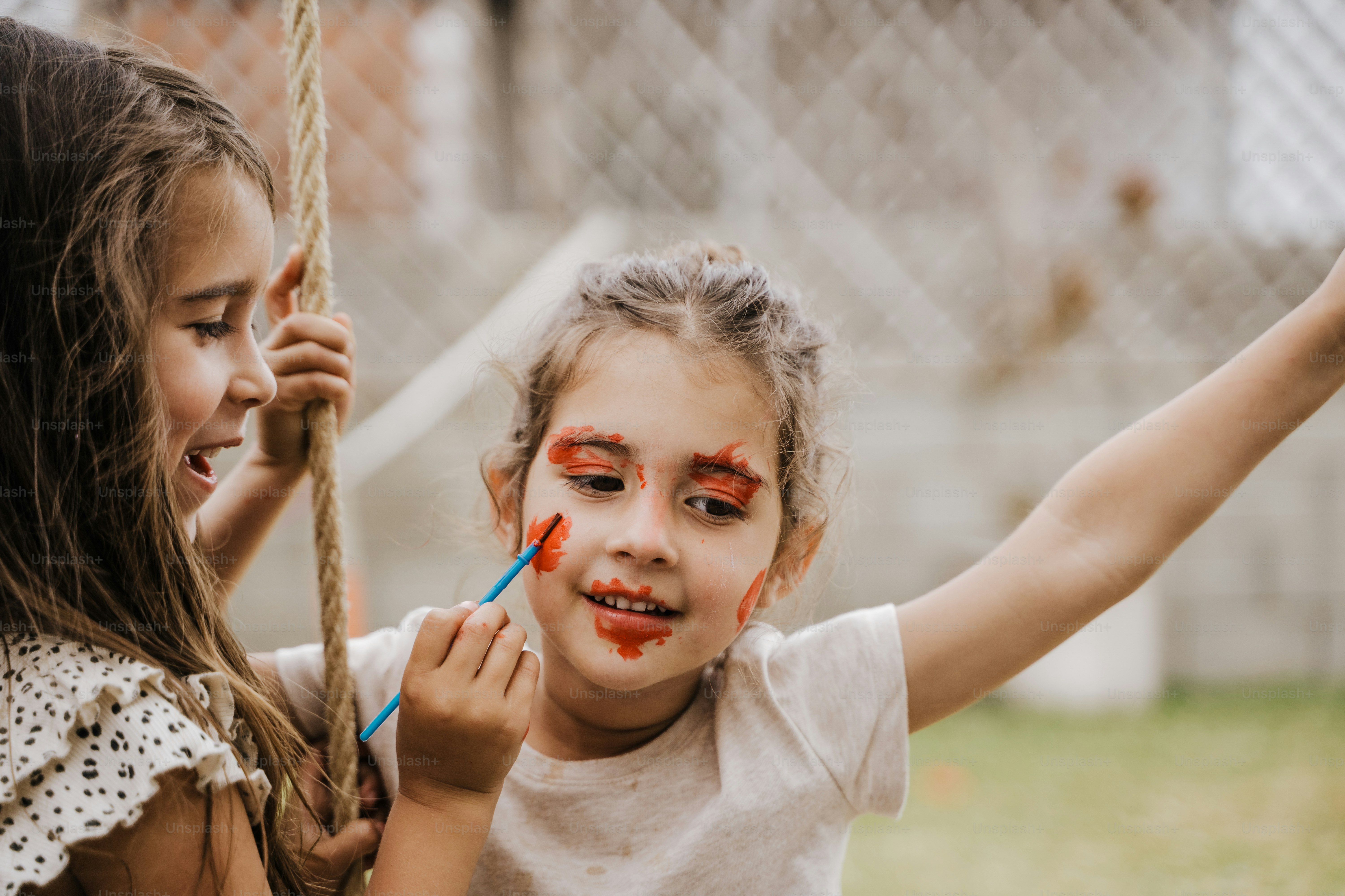 due bambine con la pittura facciale sopra che giocano su un'altalena