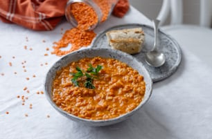 a bowl of red lentula soup with a slice of bread on the side