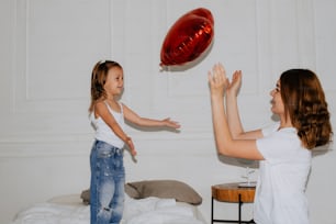 a woman holding a little girl up to a red balloon
