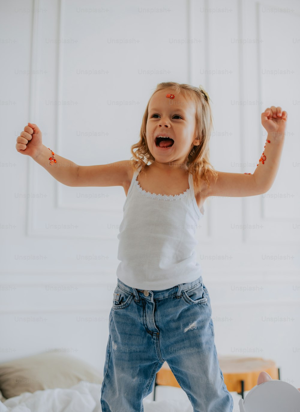 a little girl standing on a bed with her arms in the air
