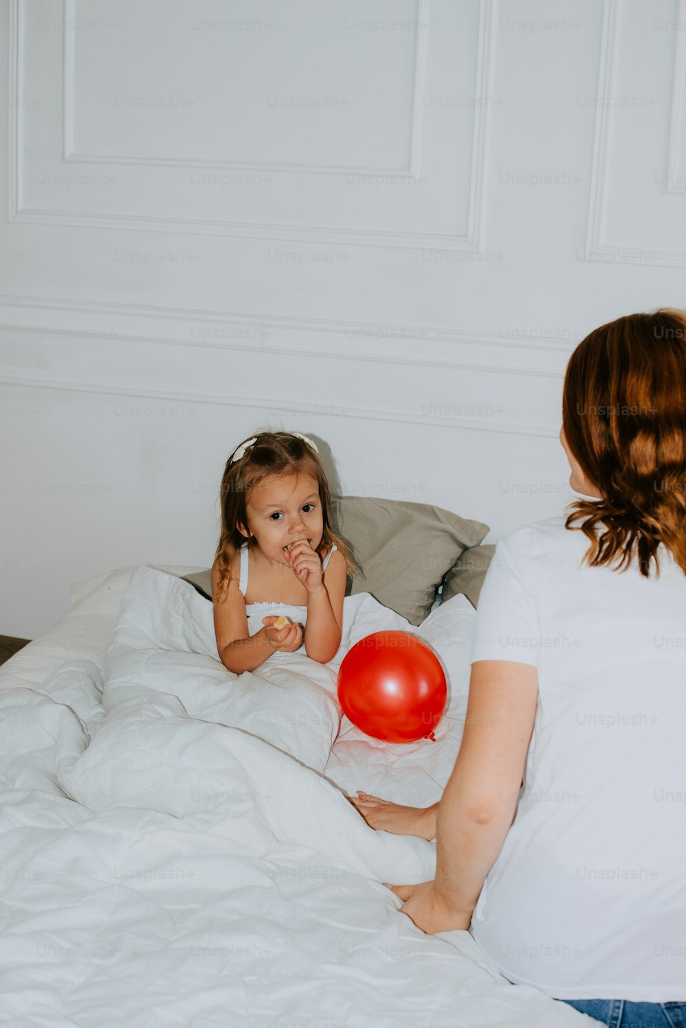a woman holding a red balloon sitting on top of a bed