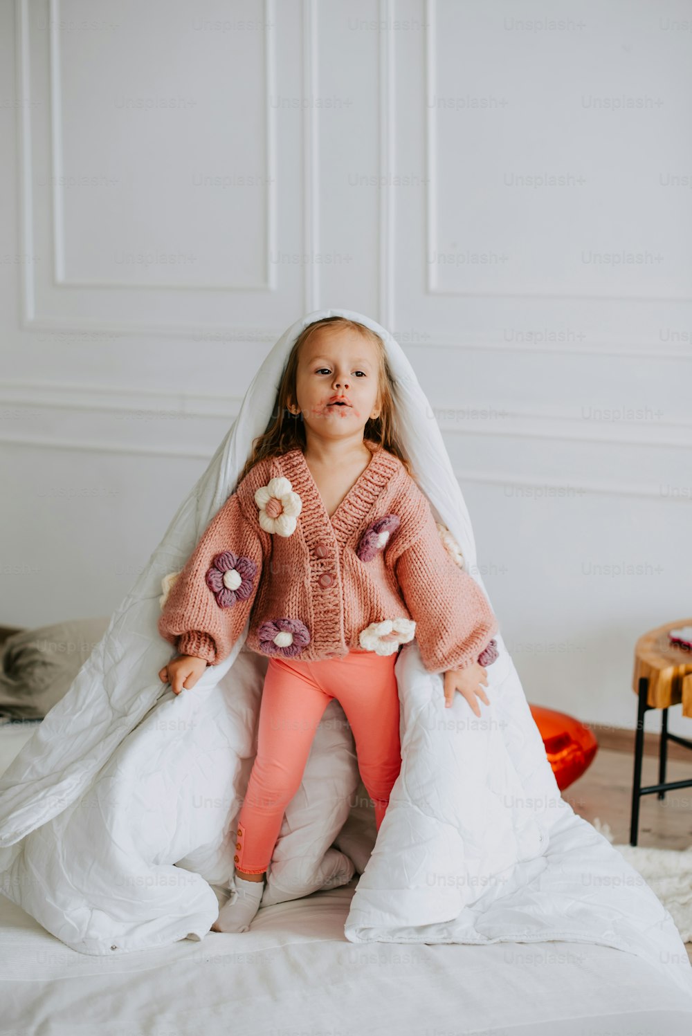 a little girl sitting on top of a bed under a blanket