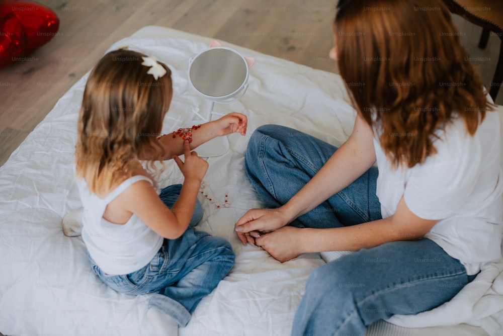 two young girls sitting on a bed playing with each other