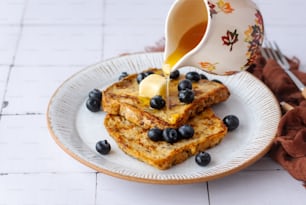 a plate of french toast with blueberries and butter being drizzled with