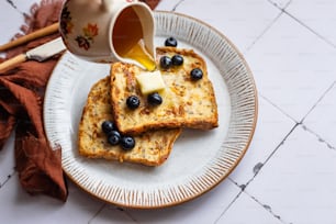 a plate of french toast with blueberries and butter being drizzled with