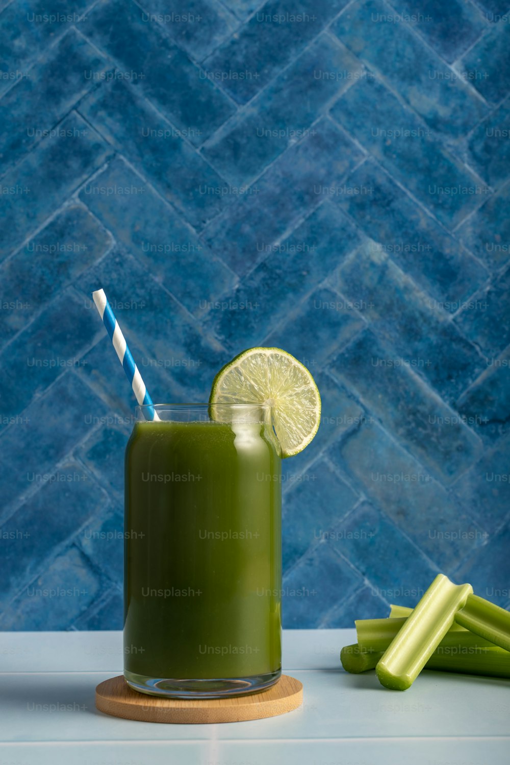 a green smoothie with a slice of lemon and a blue striped straw