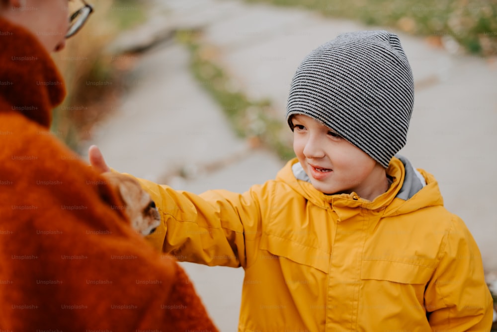 a little boy in a yellow jacket petting a cat